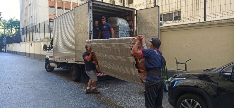 Caminhão de mudança moderno sendo carregado com móveis e caixas cuidadosamente embaladas, equipe profissional em uniformes organizando o interior com equipamentos de proteção